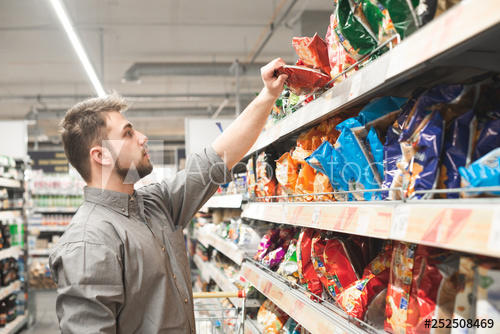 Man with a beard takes a pack of chips from the store shelves ...